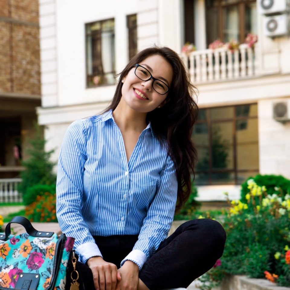 A woman in a blue striped shirt sits outdoors, smiling.