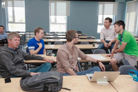 A group of people in a classroom setting, discussing and collaborating.