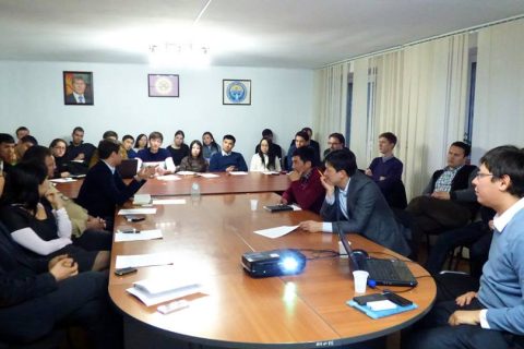 Group of people in a meeting room with a projector and laptop on a table.