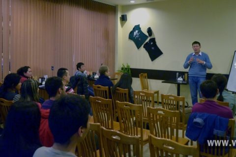 A group of people sitting in a classroom setting, listening to a speaker.