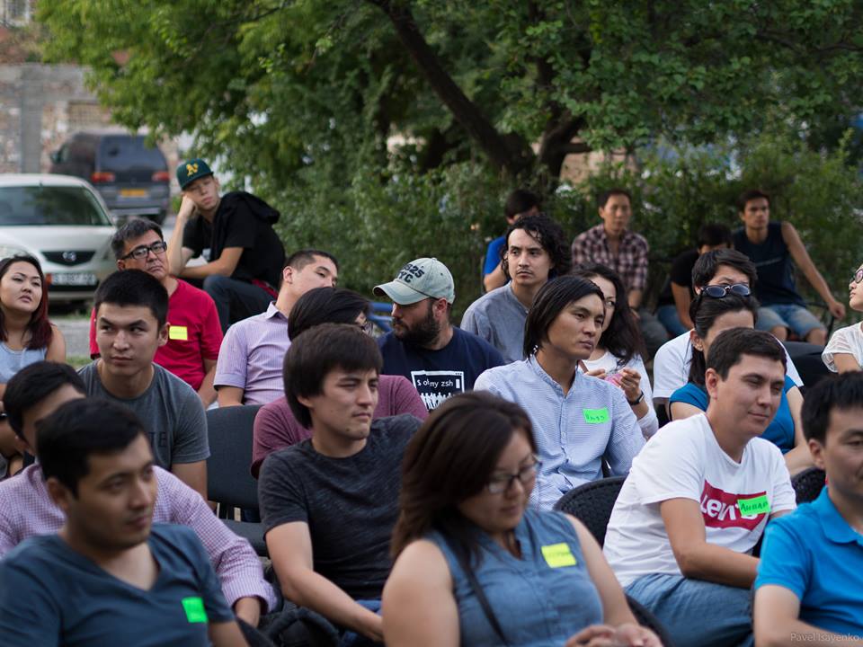 A group of people sitting outdoors, possibly attending a workshop or event.