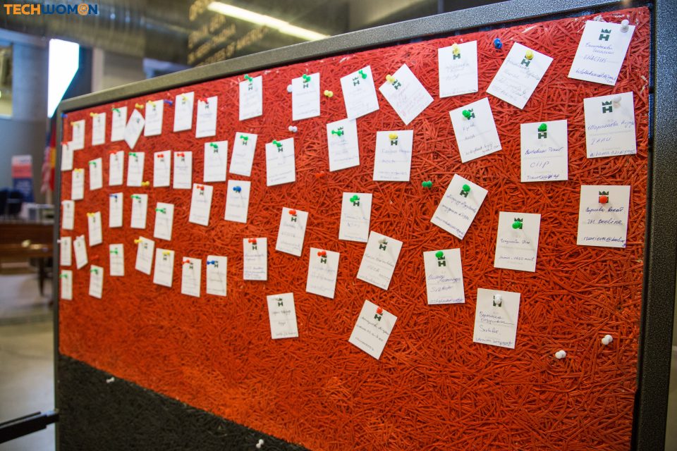 A red bulletin board with white cards pinned with colorful thumbtacks, likely used for event registration or information.
