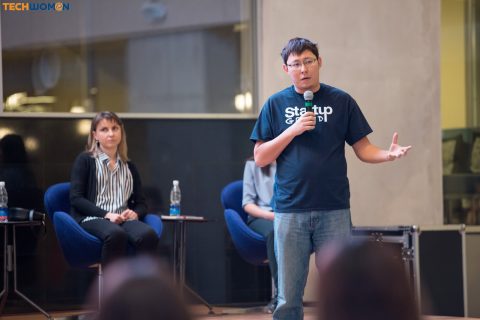 A man in a 'Startup' shirt speaks into a microphone at an event in Bishkek, Kyrgyzstan.