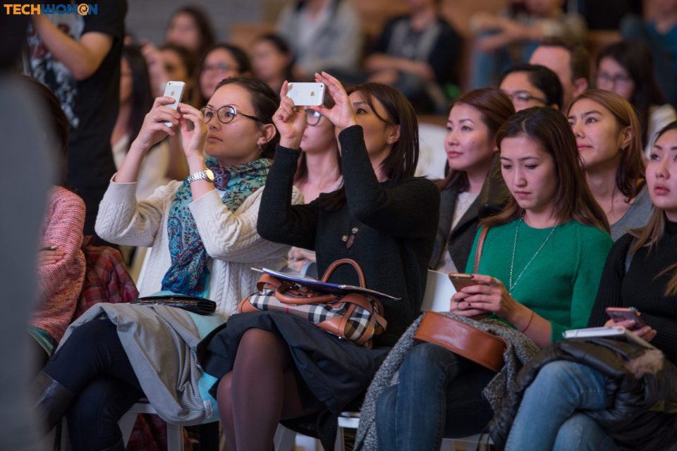 Attendees at a tech event in Bishkek, Kyrgyzstan, capturing the presentation with their smartphones.