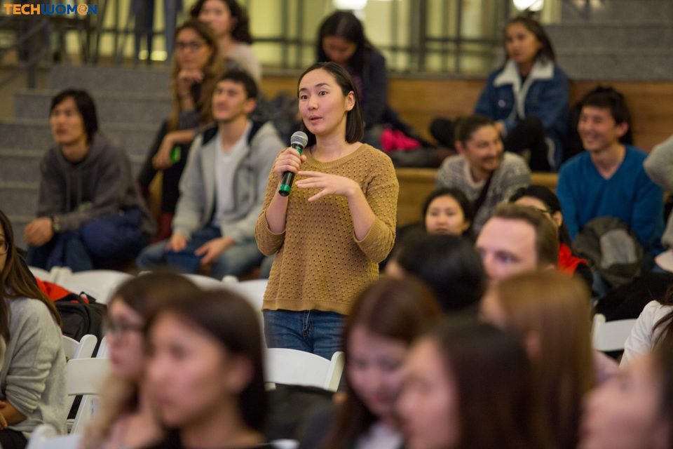 A woman speaks into a microphone in front of an audience at a tech event in Bishkek, Kyrgyzstan.