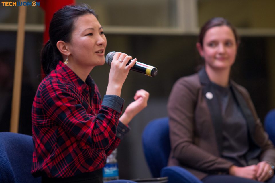 A woman in a red plaid shirt speaks into a microphone at an event in Bishkek, Kyrgyzstan.