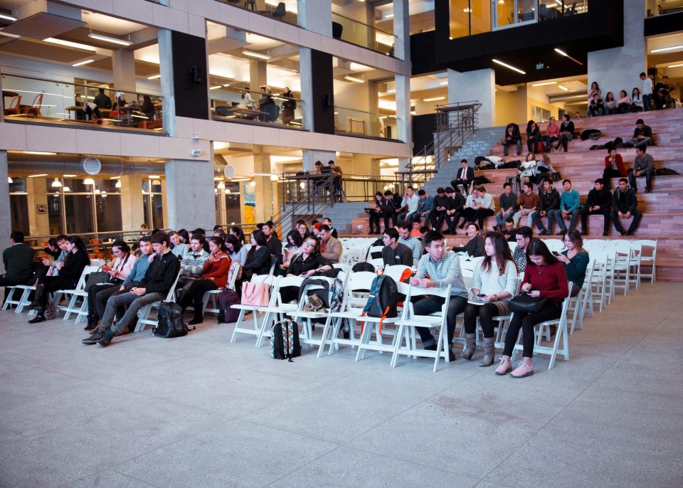 A group of people sitting in a large, modern auditorium, possibly attending an educational or informational event.
