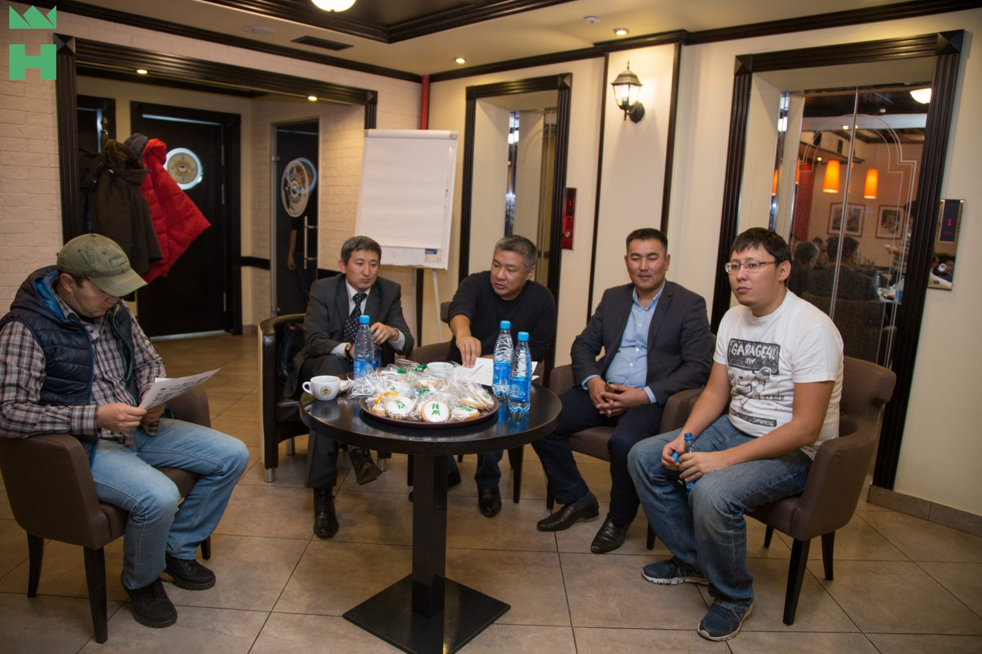 Five individuals engaged in a discussion at a roundtable in a coffee house.