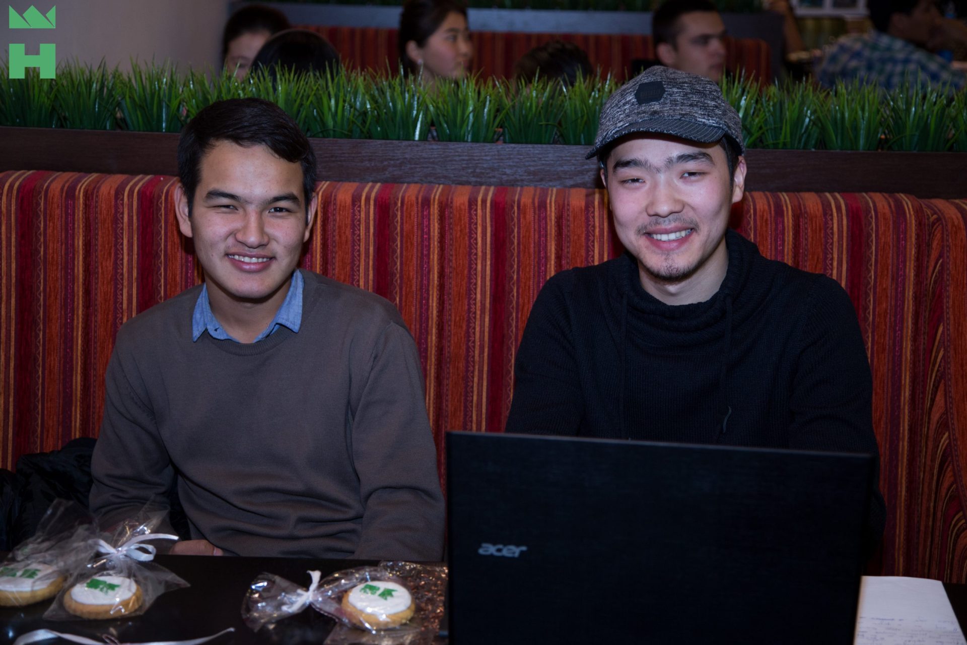Two individuals sitting at a table with an Acer laptop and cookies, in a restaurant setting.