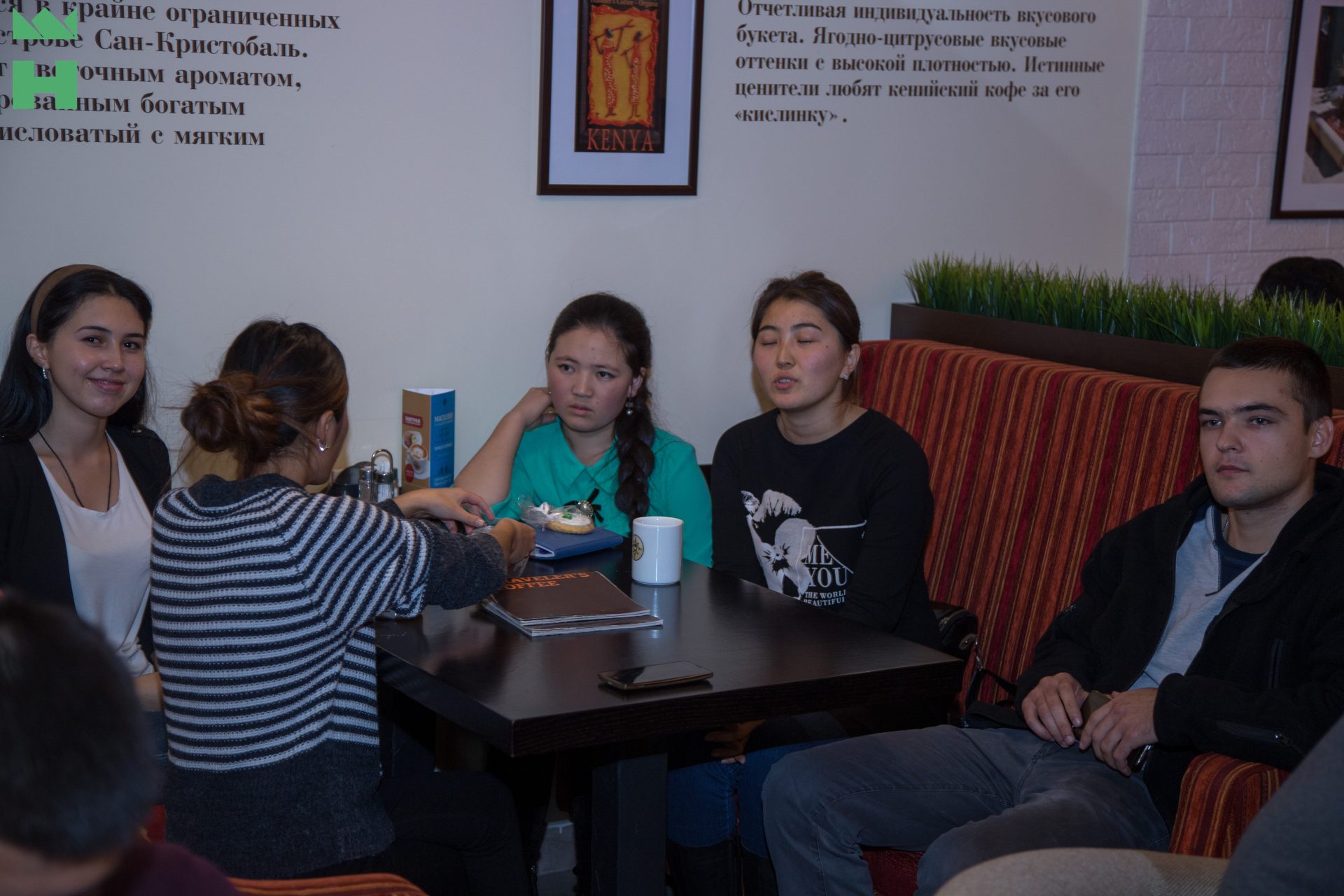 A group of people sitting around a table in a café, engaged in conversation.
