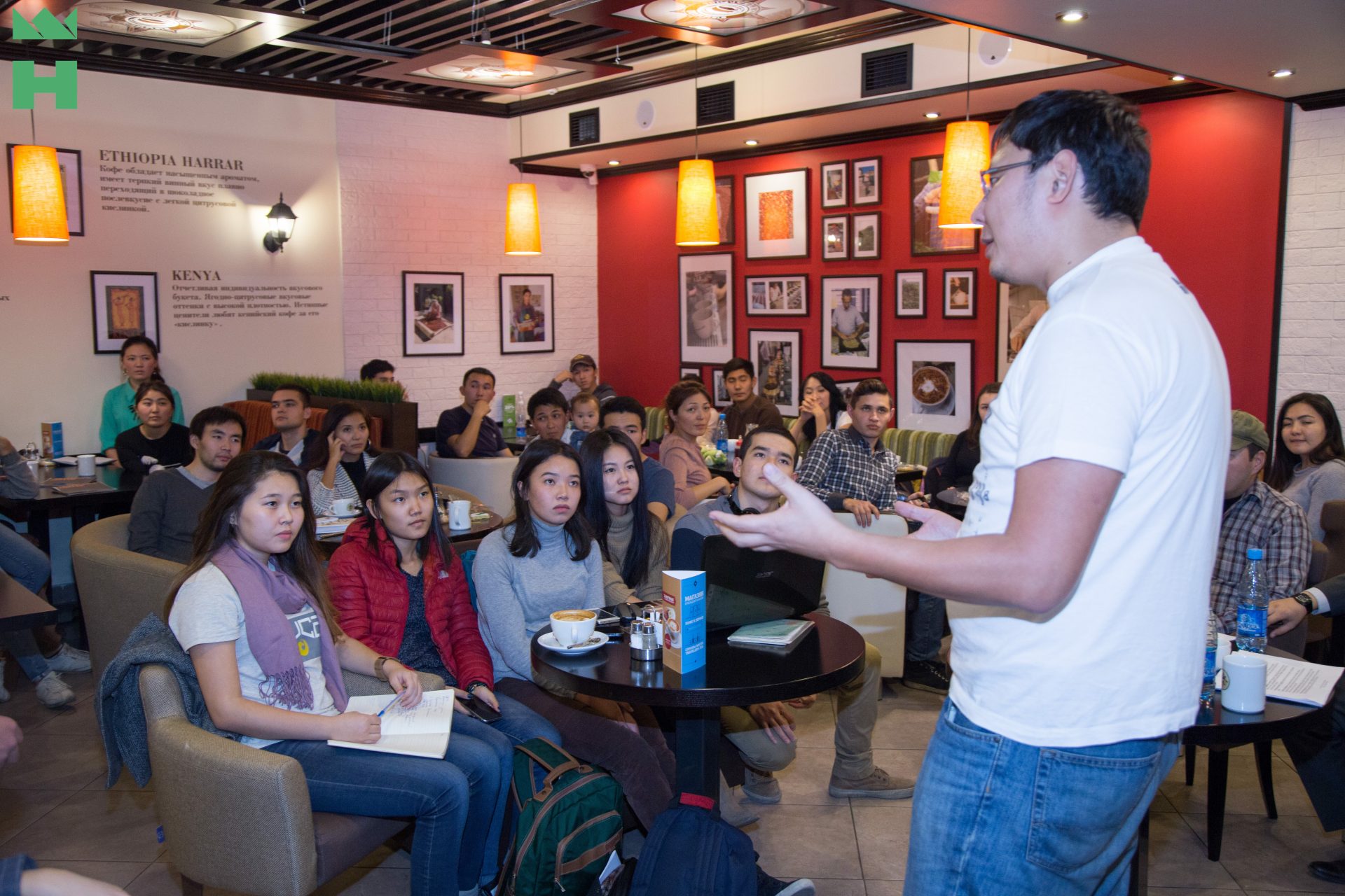A group of people is gathered in a café for a workshop or training session.