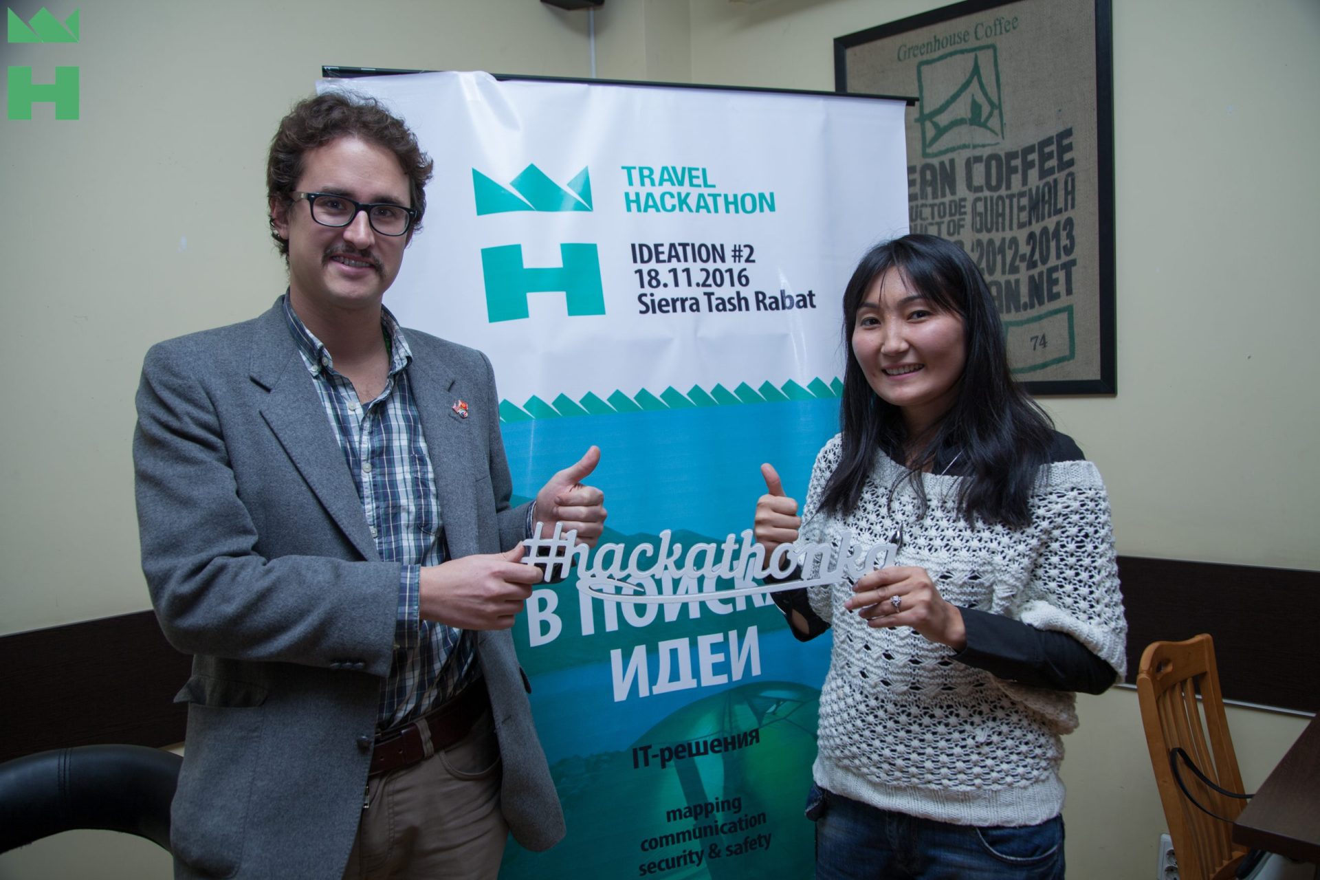 Two individuals holding a sign with the hashtag #hackathon at a Travel Hackathon event in Bishkek, Kyrgyzstan.