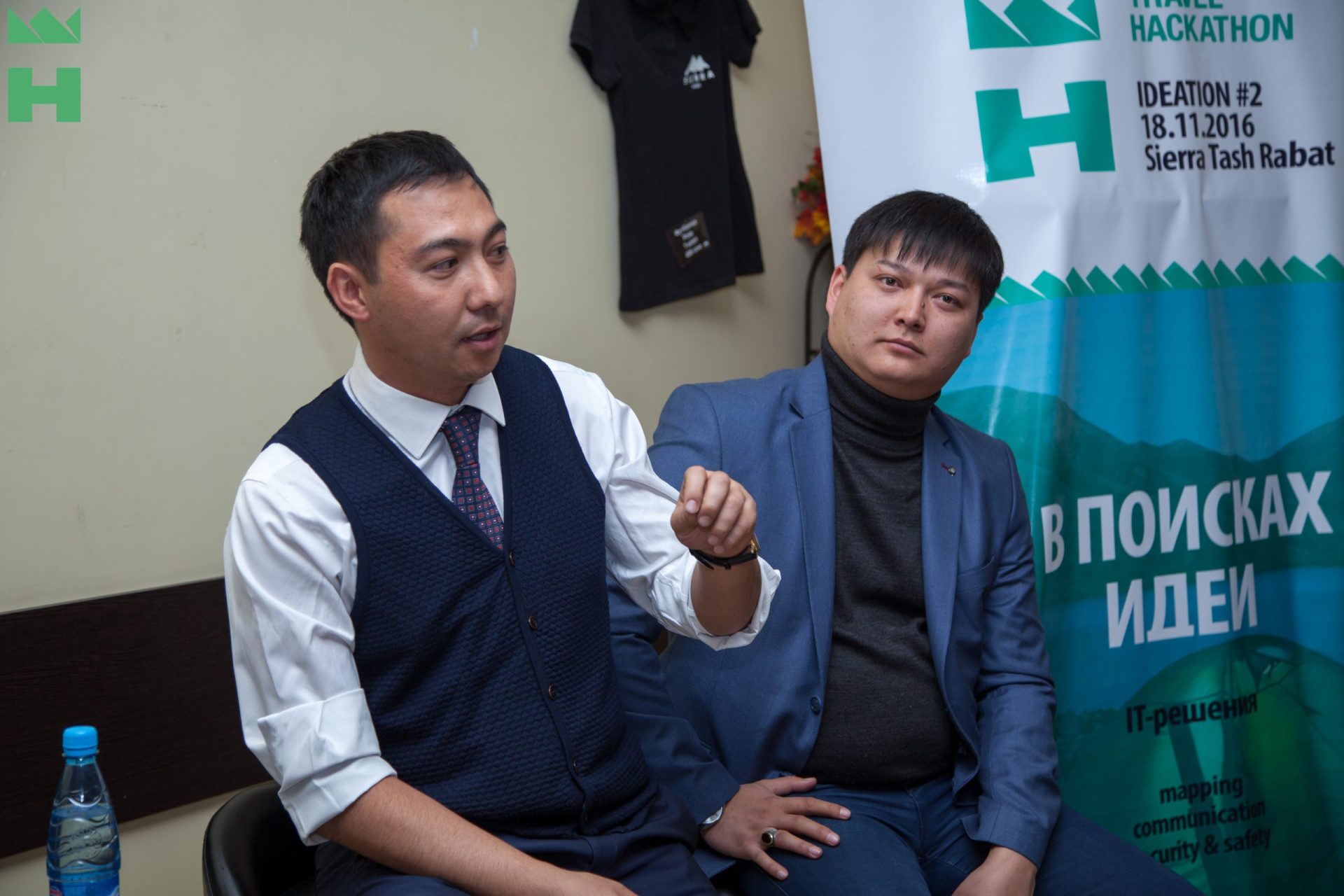 Two men in formal attire are seated in front of a banner that reads 'Travel Hackathon Ideation #2 18.11.2016 Sierra Tash Rabat'.