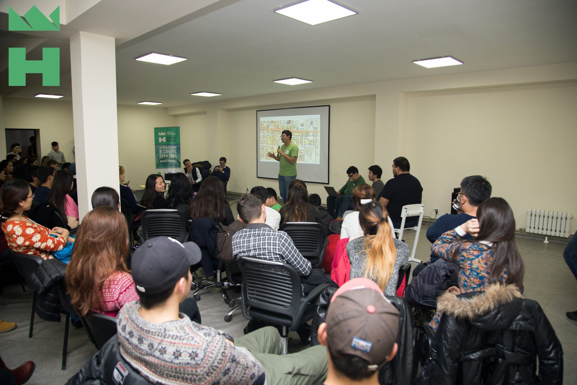 A group of people sitting in a room, listening to a presentation on a map projected on a screen.