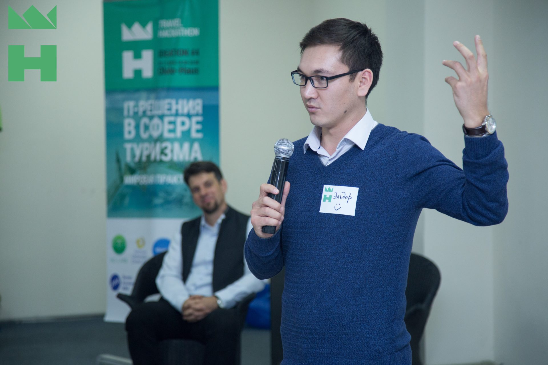 A person speaking at an event with a banner in the background.