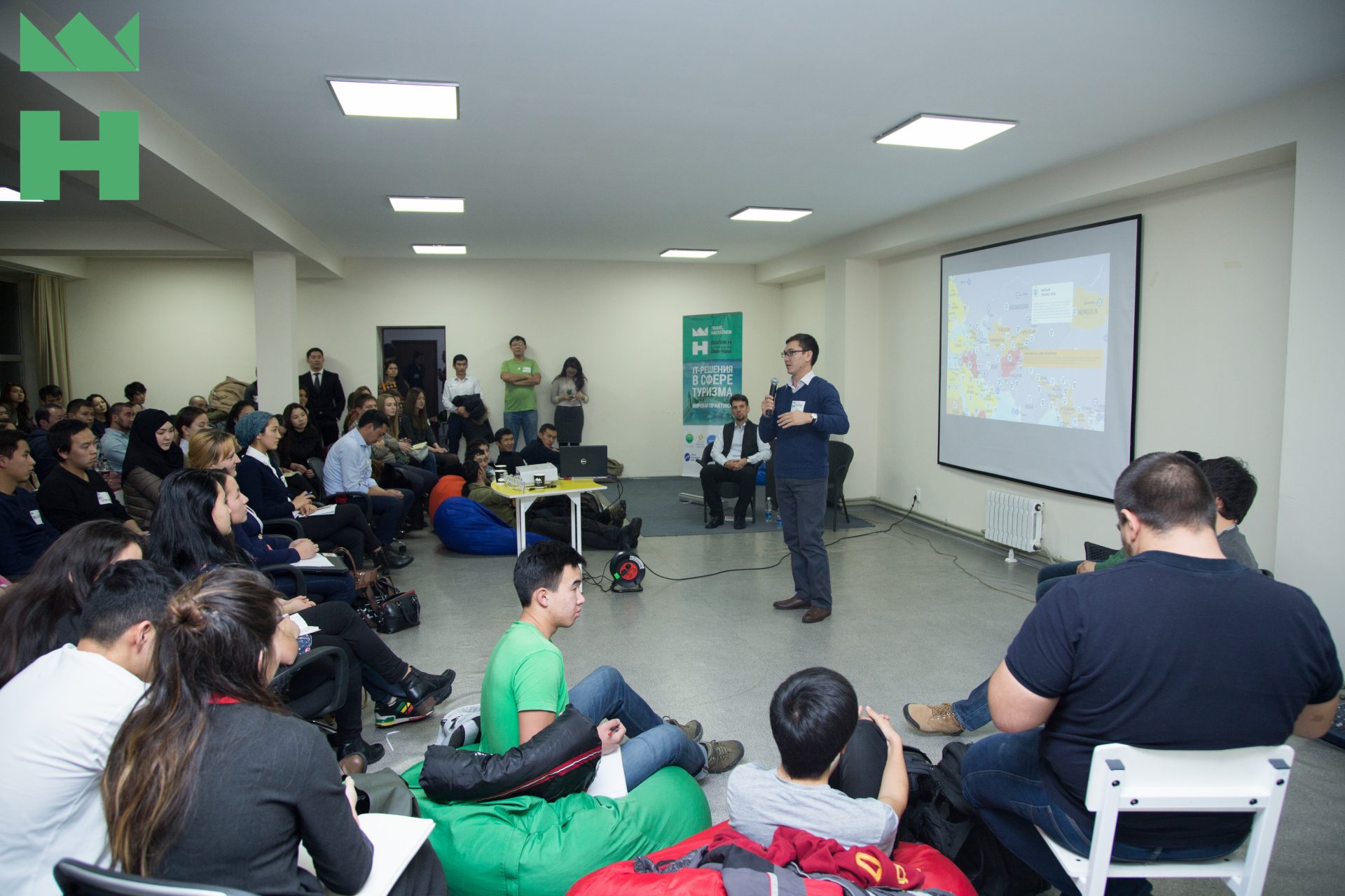 A group of people sitting on bean bags and chairs in a room with a projector screen displaying a map.