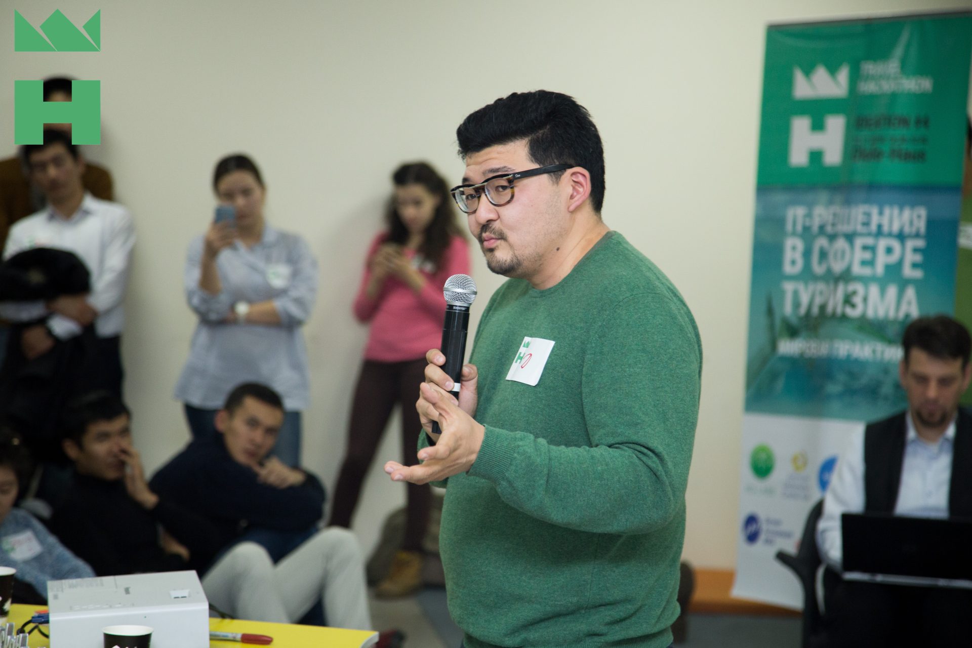 A person in a green sweater speaks into a microphone at a workshop in Bishkek, Kyrgyzstan.