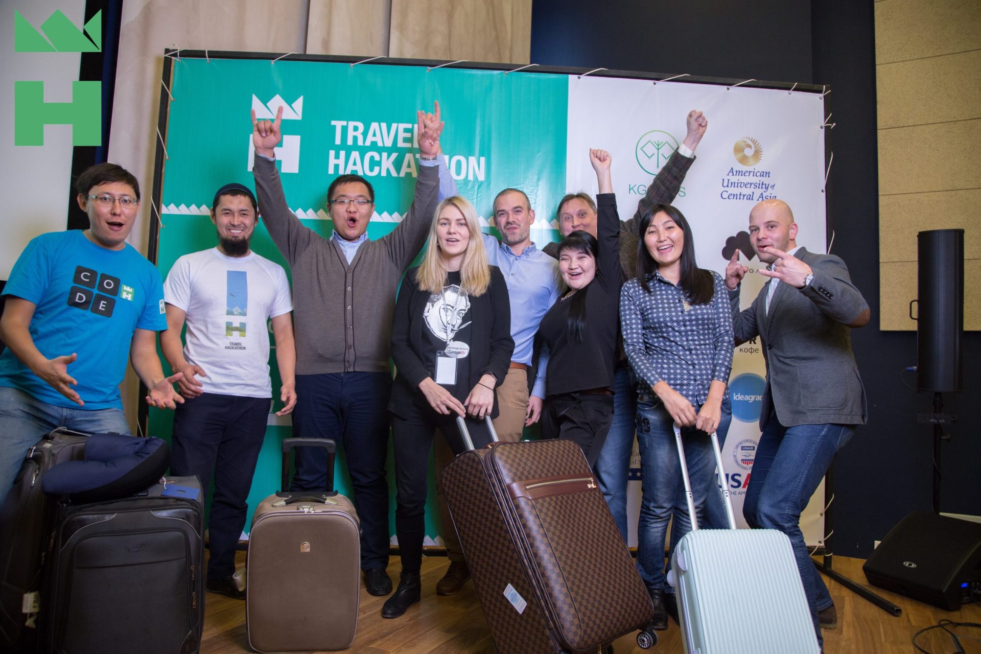 Participants at a Travel Hackathon event in Bishkek, Kyrgyzstan, celebrating with raised hands and luggage.
