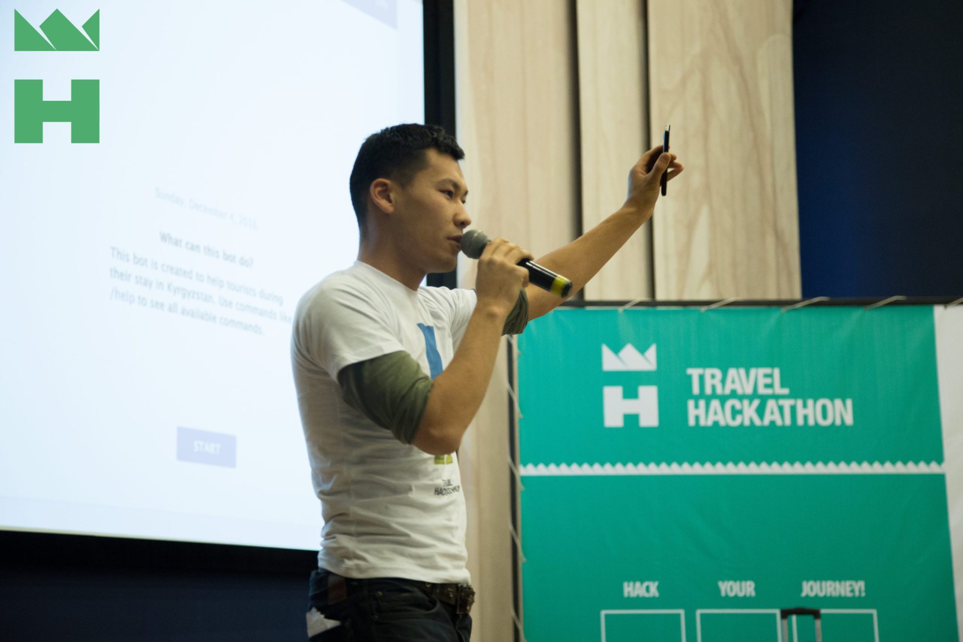 A person speaking into a microphone at a Travel Hackathon event in Bishkek, Kyrgyzstan.
