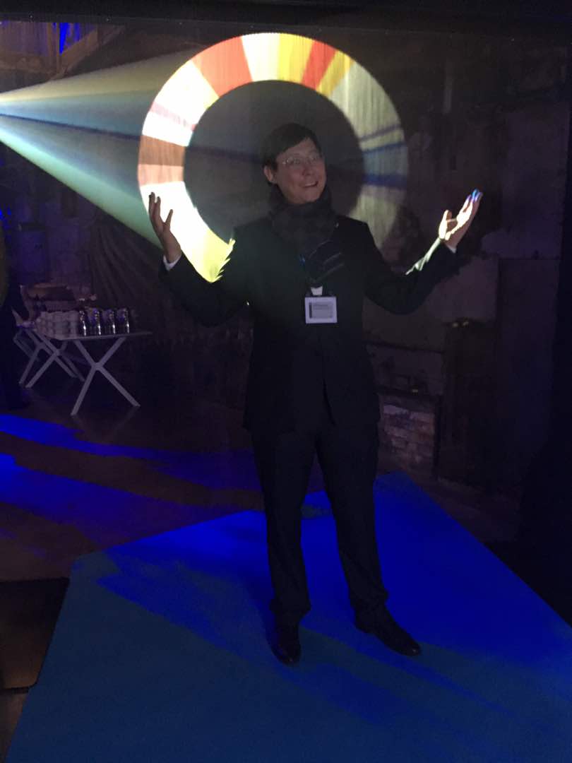A person in a suit stands with arms outstretched in front of a colorful light projection.