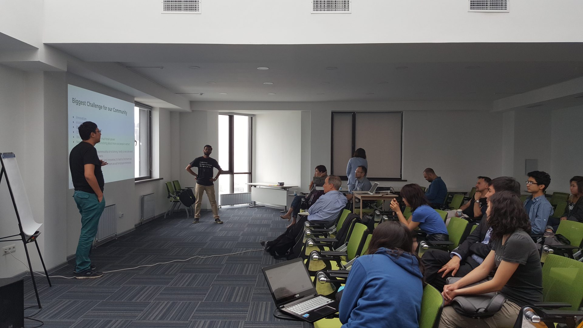 Two presenters addressing a group of workshop attendees in a conference room.