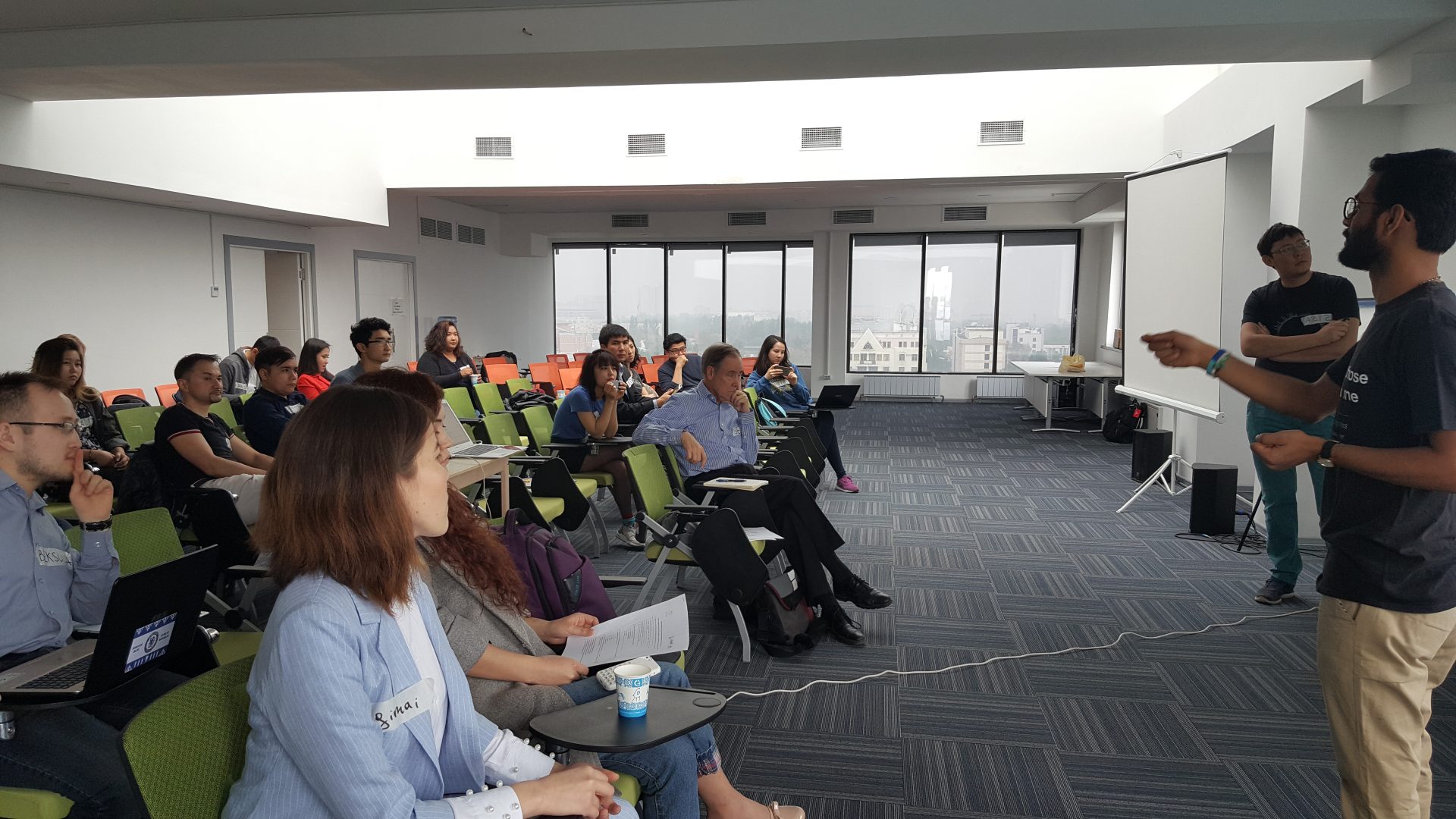 Participants in a workshop or training session in a modern, well-lit room with a presenter at the front.