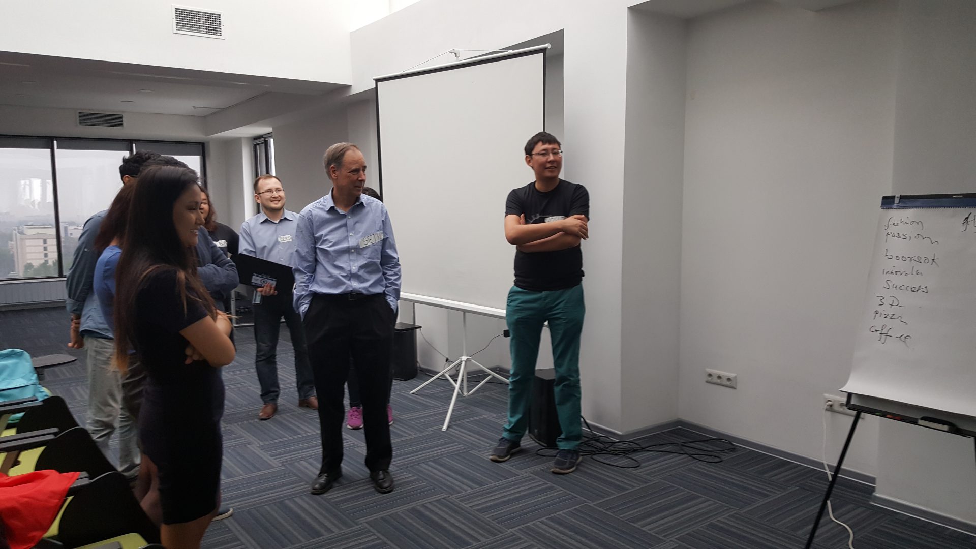 A group of people standing in a conference room with a whiteboard and projector screen.