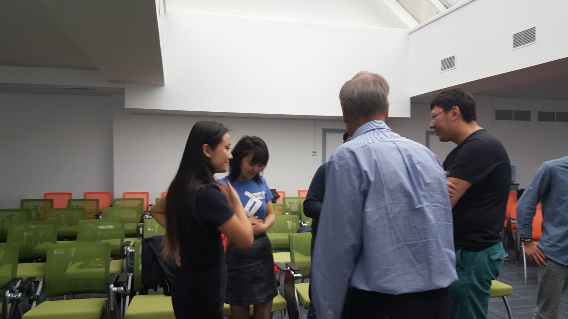 A group of people standing in a classroom setting, engaged in a discussion.