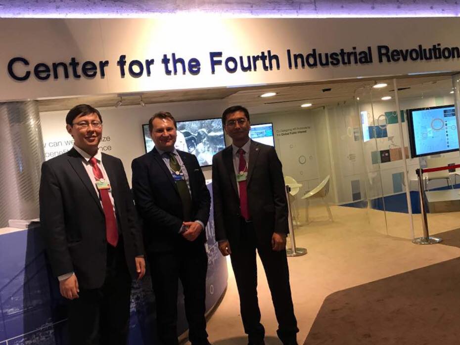 Three men in suits stand in front of a sign for the Center for the Fourth Industrial Revolution.