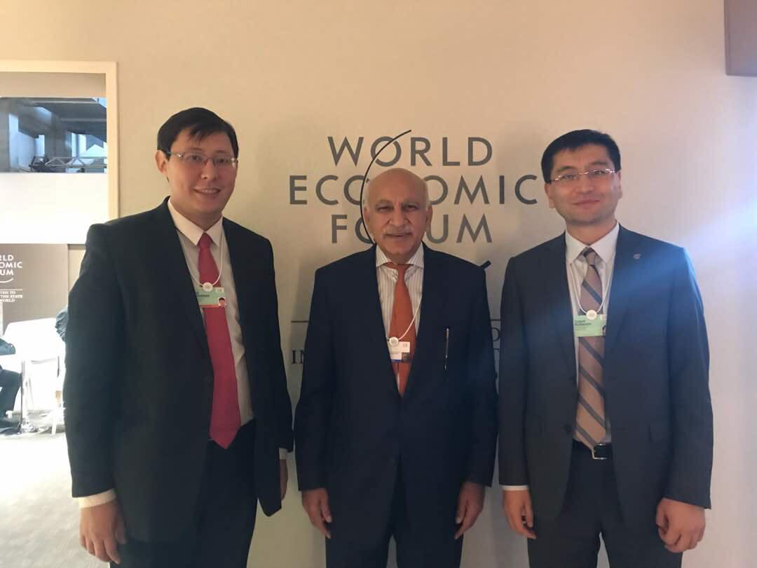 Three men in suits pose for a photo in front of a World Economic Forum sign.