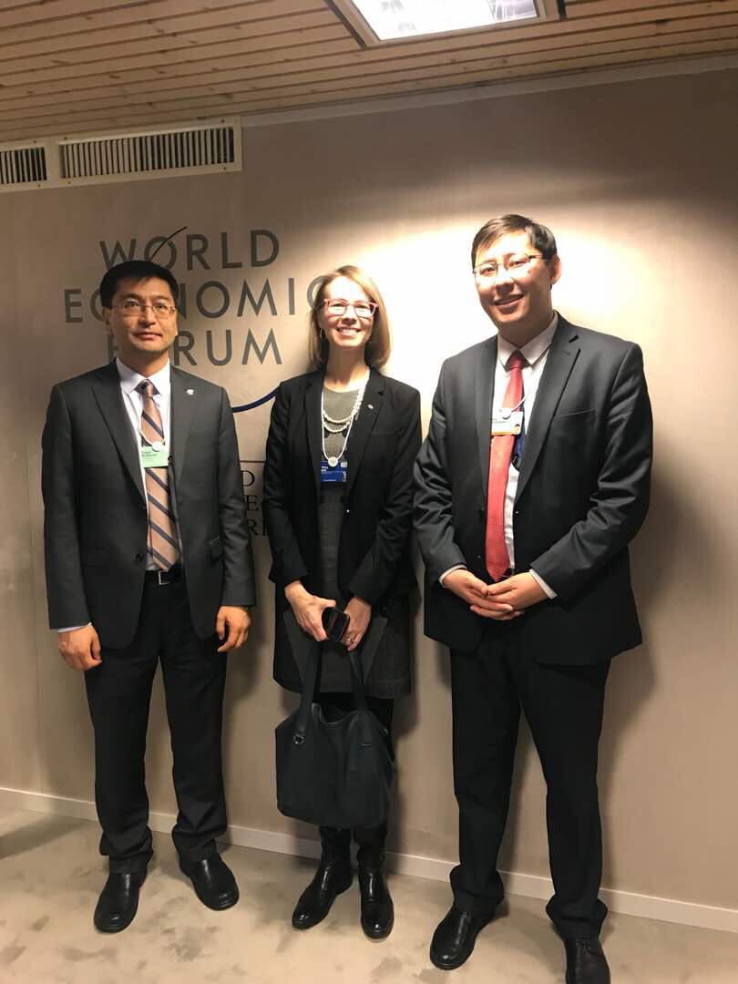 Three individuals pose for a photo in front of a World Economic Forum backdrop.
