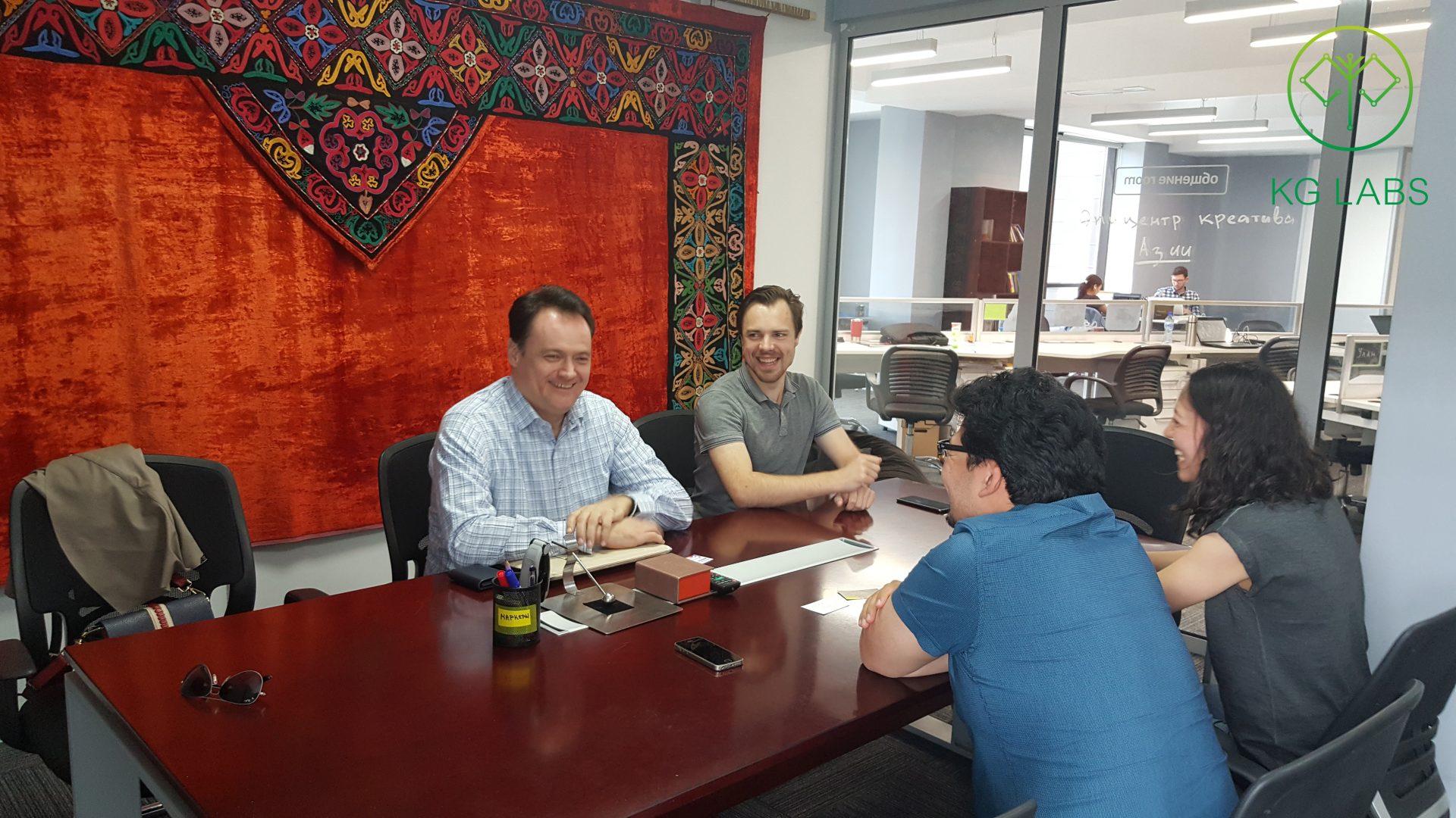 Four individuals engaged in a meeting at a conference table in a modern office setting.