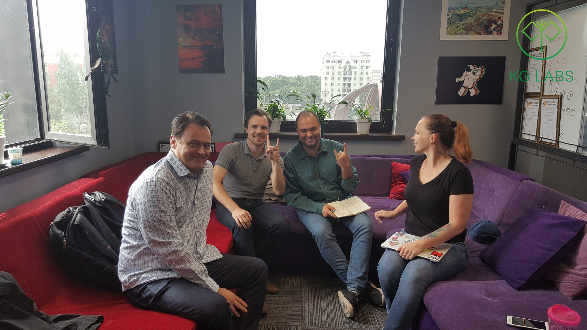 Four individuals sitting on a couch in a modern office setting, engaged in a casual discussion.