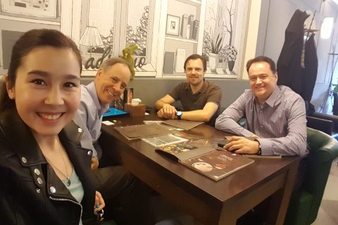 Four individuals sitting at a table in a cafe with menus and papers.