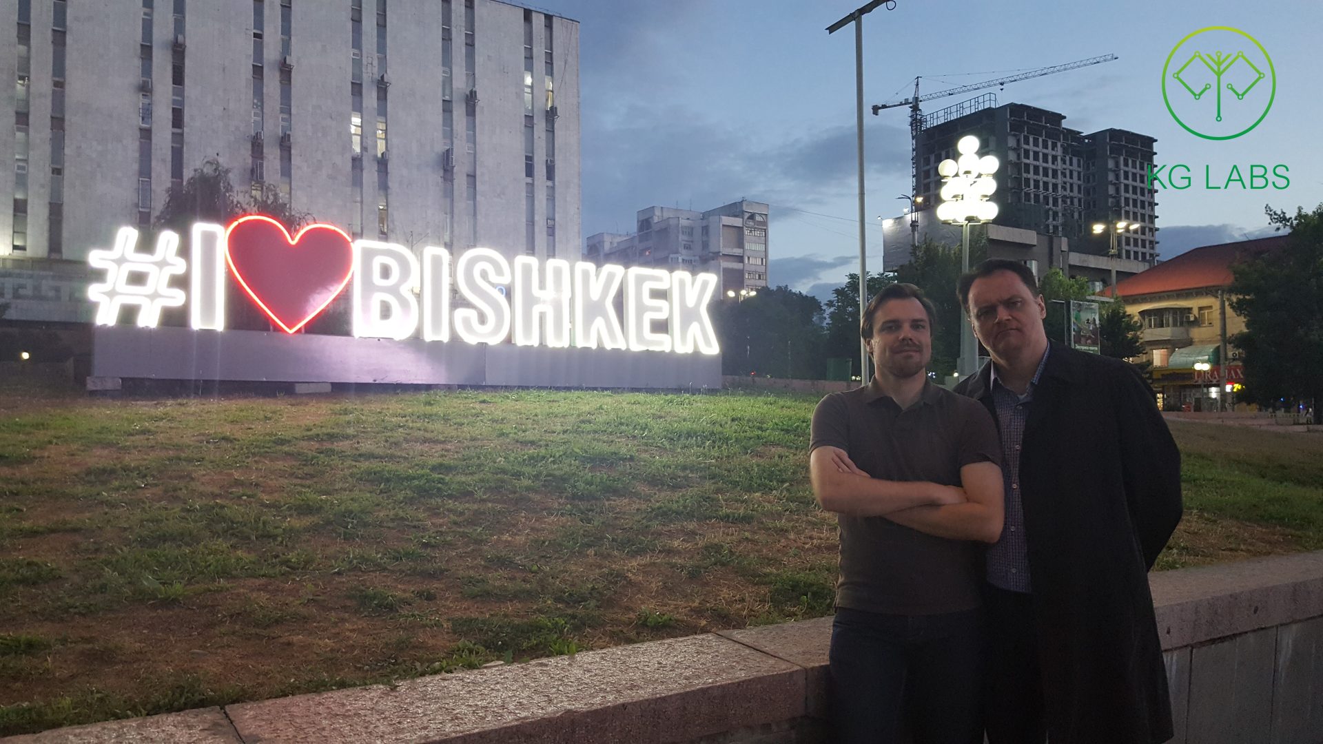 Two individuals posing in front of a illuminated sign that reads '#I love Bishkek' in Bishkek, Kyrgyzstan.