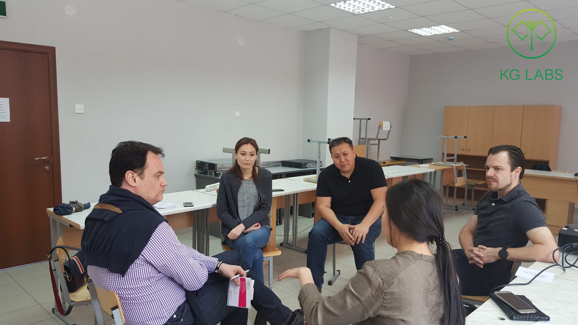A group of five people engaged in a discussion in a classroom setting at KG Labs Foundation in Bishkek, Kyrgyzstan.