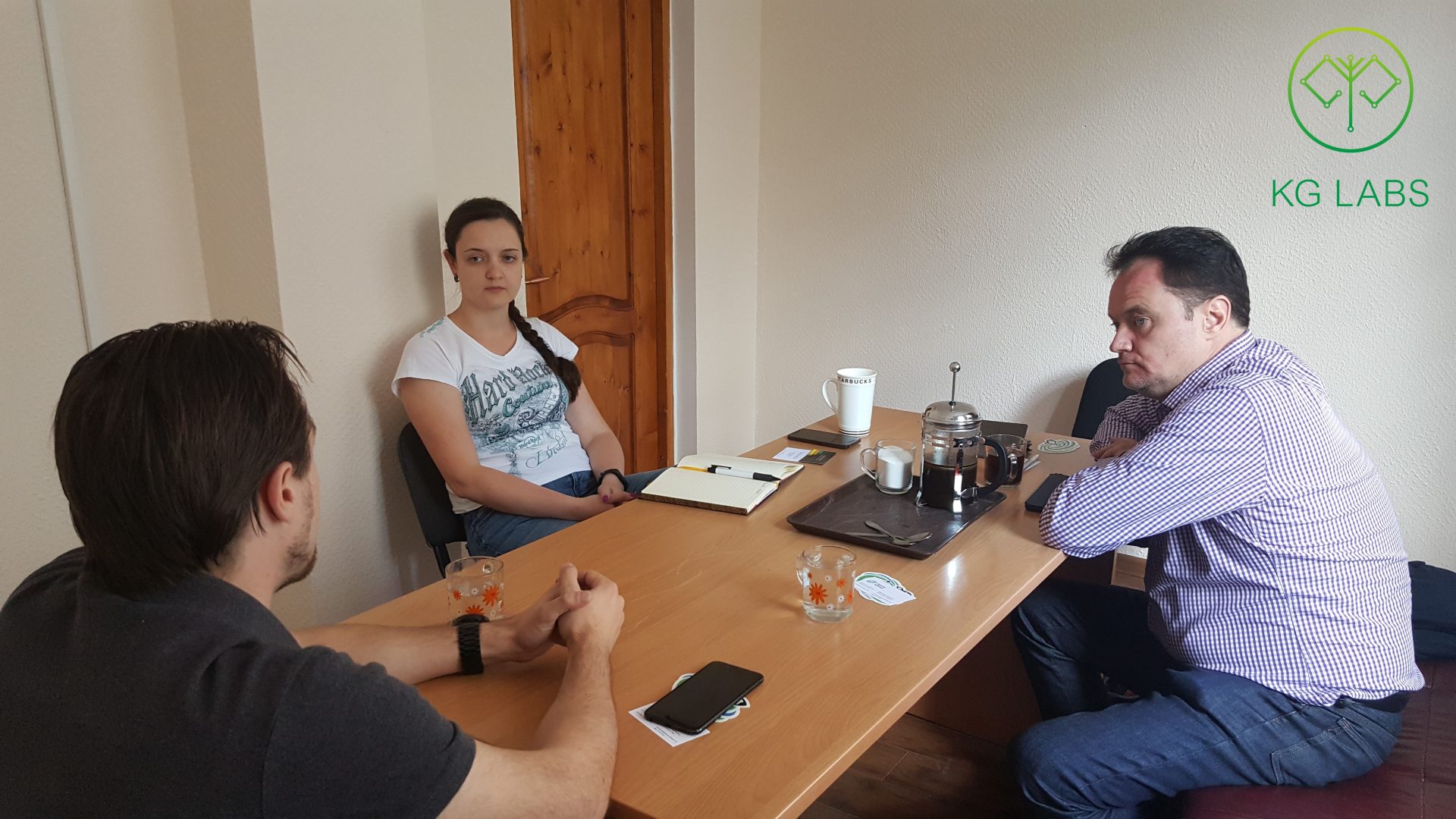 Three individuals engaged in a meeting at a table in a room with a door in the background.