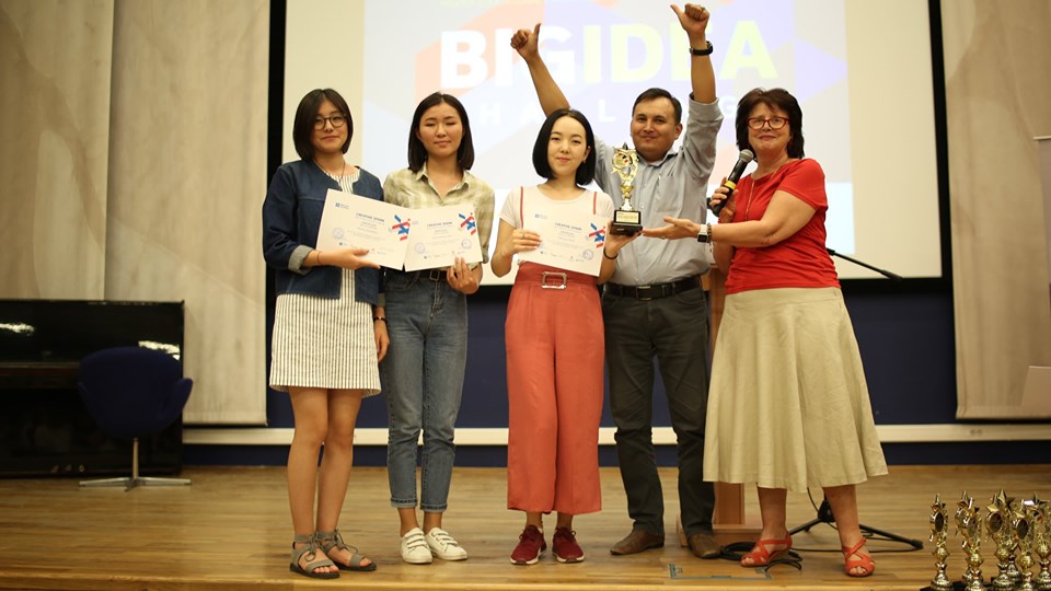 A group of people on stage holding certificates and a trophy, likely at an award ceremony.