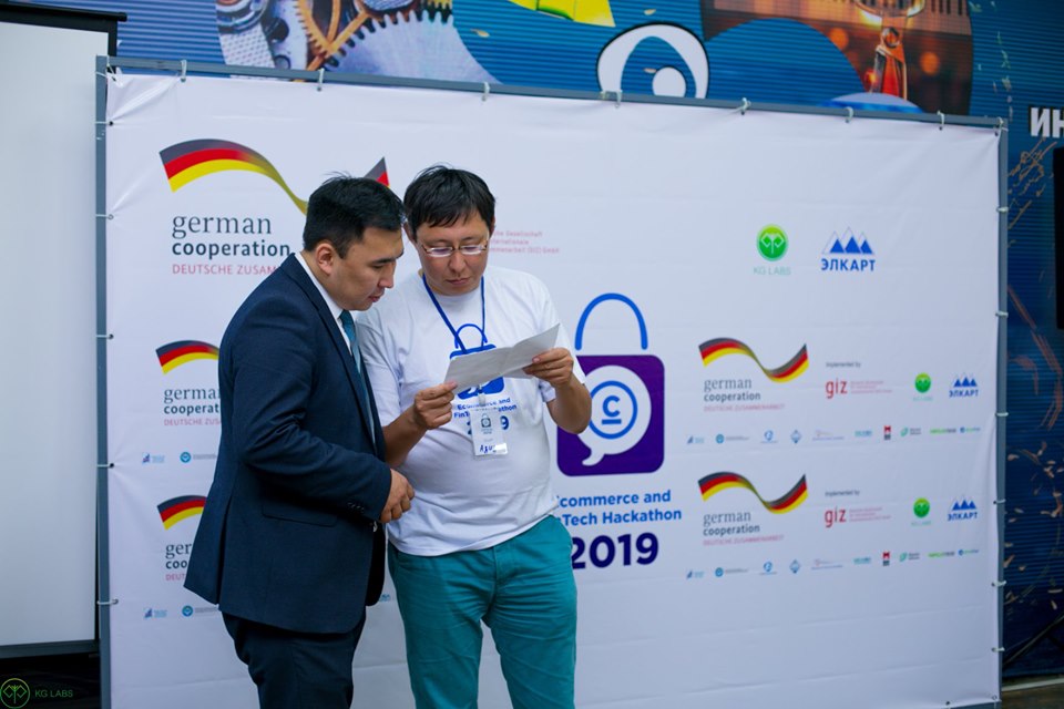 Two individuals discussing a document at the E-commerce and FinTech Hackathon 2019 in Bishkek, Kyrgyzstan.
