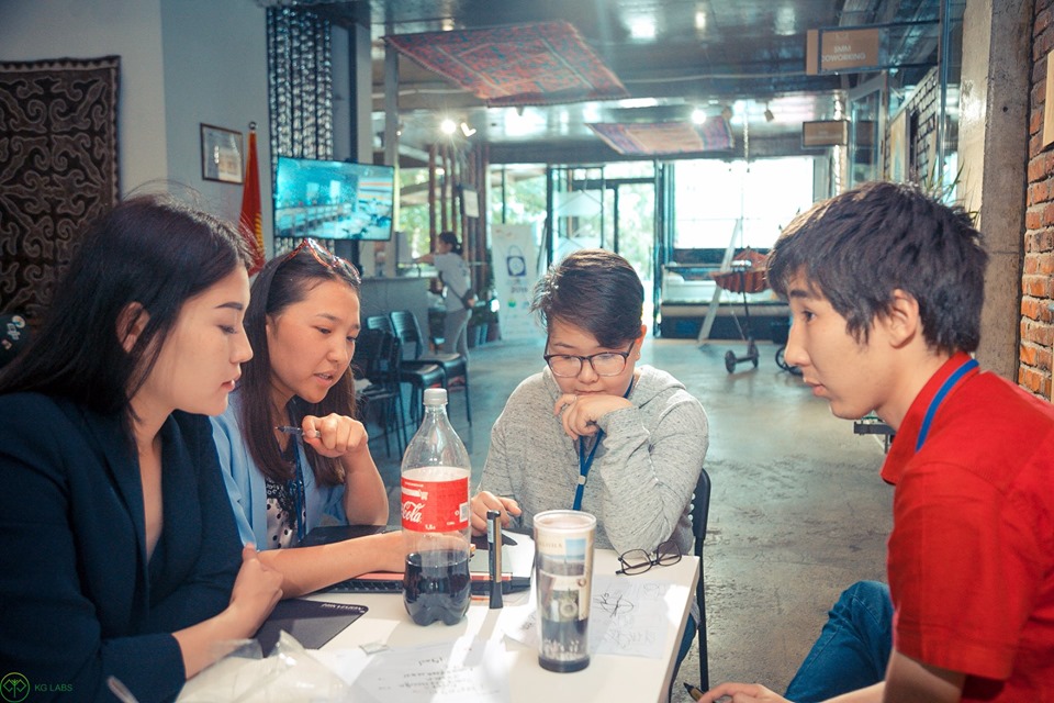 A group of young people working together at a table in a modern office setting.